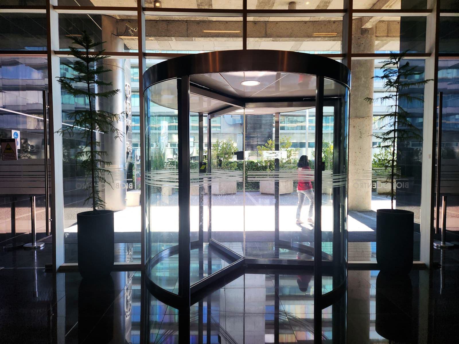 Acceso de edificio corporativo con coníferas en maceteros junto a la puerta giratoria
