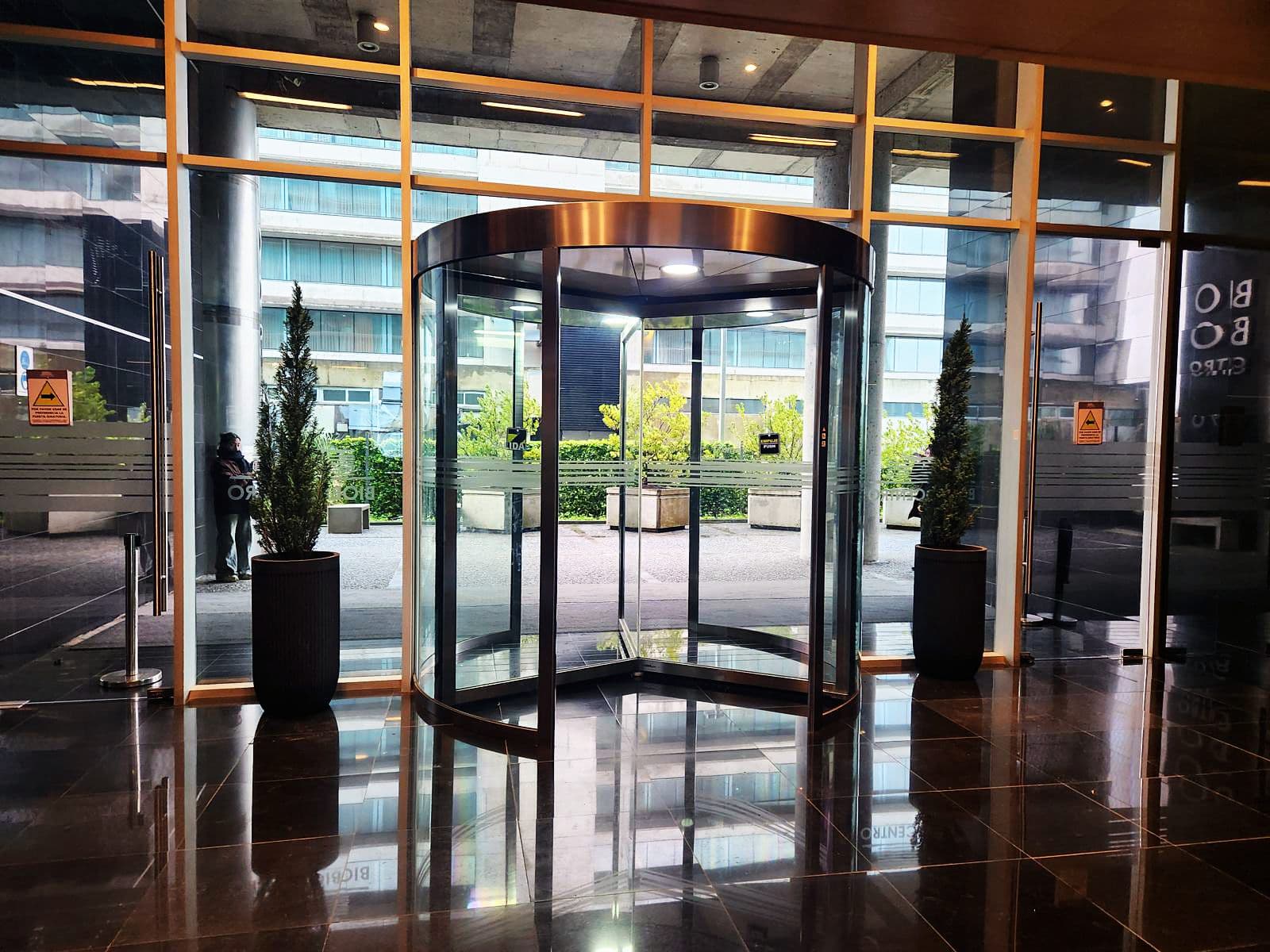 Acceso de edificio con coníferas flanqueando la puerta giratoria